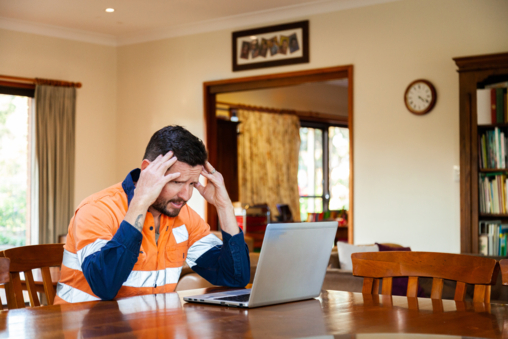 Stressed tradie reviewing invoices and financial reports on computer, highlighting the importance of good bookkeeping.